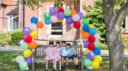 Pre-prep children sat on a bench under a balloon arch outside at Great Walstead